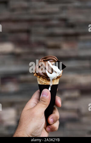 Mann mit Vanille und Schokolade schmelzen von Eis in der Hand, Erdnüsse Kegel herum, sehr unscharfen Hintergrund, kleine Tiefenschärfe. Der dunkle Hintergrund. Stockfoto