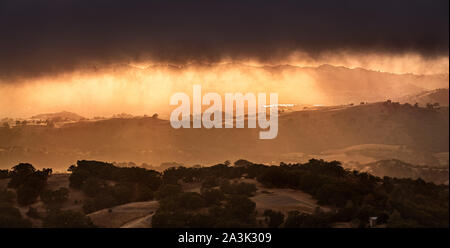 Düstere und bedrohliche Sturm Wolken am Himmel bei Sonnenuntergang; hell orange leuchtenden Hügel und Täler in South San Francisco Bay Area, San Jos Stockfoto