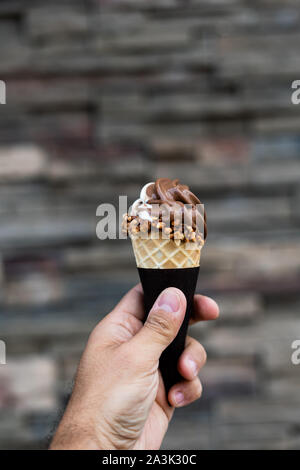 Mann mit Vanille und Schokolade Eis in der Hand, Erdnüsse Kegel herum, sehr unscharfen Hintergrund, kleine Tiefenschärfe. Der dunkle Hintergrund. Stockfoto