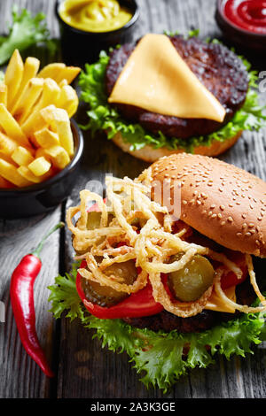 Drei Cheeseburger mit rindfleischpastetchen, Cheddar Käse, knusprig gebratenen Zwiebeln, Salat, Tomaten, Gurken in Scheiben geschnitten auf einem rustikalen Holztisch mit Senf ein Stockfoto