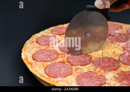 Hand und Pizza Salami mit Messer auf schwarzem Hintergrund Stockfoto