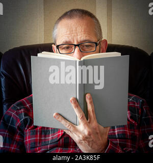 Ein senior Mann mit Bart und Brille, auf dem Sofa sitzen und ein Buch zu lesen Stockfoto