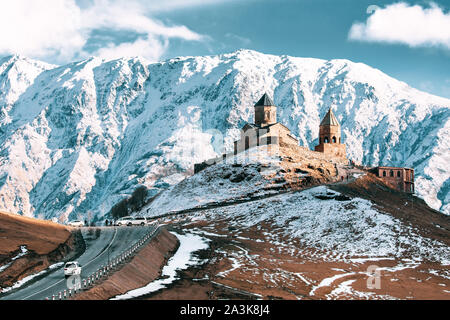 Stepantsminda, Gergeti, Georgia. Berühmte Gergeti Trinity Tsminda Sameba Kirche im frühen Winter Landschaft. Suv-Umzug in der Nähe von Kirche in schönen georgianischen Stockfoto