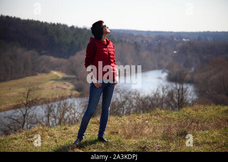 Ein Mädchen sammelt Schneeglöckchen im Wald. Schöne junge Frau taucht in den Strahlen der Frühlingssonne auf einer Lichtung im Wald. Stockfoto