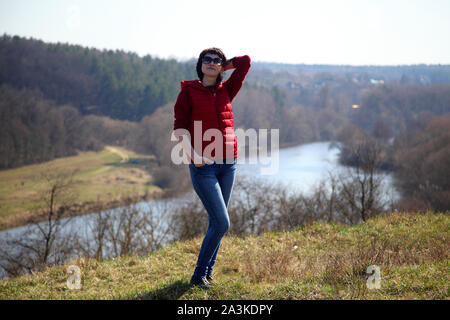 Ein Mädchen sammelt Schneeglöckchen im Wald. Schöne junge Frau taucht in den Strahlen der Frühlingssonne auf einer Lichtung im Wald. Stockfoto