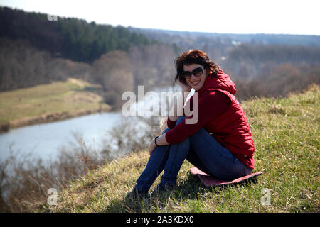 Ein Mädchen sammelt Schneeglöckchen im Wald. Schöne junge Frau taucht in den Strahlen der Frühlingssonne auf einer Lichtung im Wald. Stockfoto