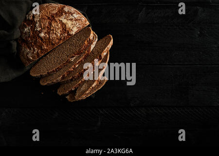 Geschnittenes Brot auf schwarzem Holz- Hintergrund. Köstliche, frisch gebackenem Brot. Ansicht von oben. Kopieren Sie Platz. Stockfoto