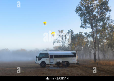 Ein Toyota Coaster Reisemobil lagerten bei Sonnenaufgang im Busch mit gelben Heißluft-Ballone Overhead, Mareeba, Queensland, Queensland, Australien Stockfoto