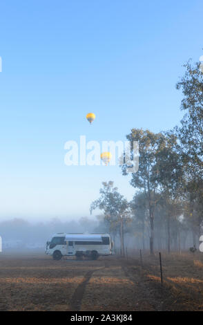 Vertikale Ansicht eines Toyota Coaster Reisemobil lagerten bei Sonnenaufgang im Busch, mit gelben Heißluft-Ballone Overhead, Mareeba, Queensland, Queensland, Australien Stockfoto