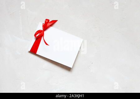 White paper Hinweis Grußkartenvorlage mit roter Schleife auf weiße strukturierte Hintergrund. Flach, Ansicht von oben, kopieren Raum Stockfoto