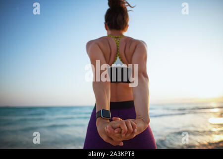 Hinter der jungen Frau im Sport Fitness Kleidung am Strand bei Sonnenuntergang stretching gesehen. Stockfoto