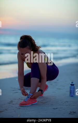 Fitness Frau in Sport Kleidung am Meer am Abend Schnürsenkel binden. Stockfoto