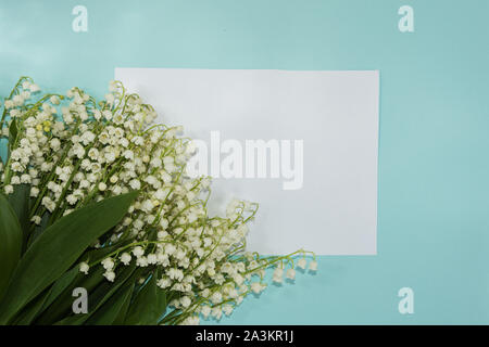 Eine leere Karte und Maiglöckchen Blumen auf dem Pastell hellen Hintergrund. Mockup für Design. Grußkarte. Stockfoto