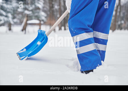 7/8-Ansicht der Arbeiter der Stadt service im Prozess der Schneeräumung von Straßen im Winter. Mann mit blauen Uniform halten Schaufel und Reinigung der Bürgersteige im Morgen. Konzept der Wartung. Stockfoto