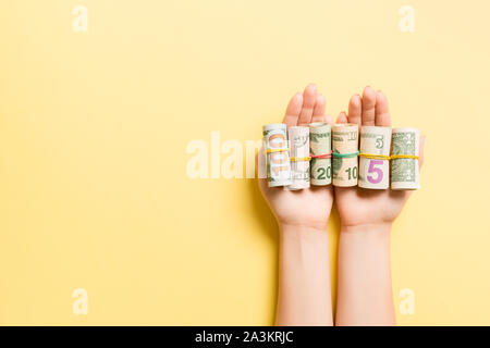 Blick von oben auf die weibliche Hände halten eine Menge aufgerollt Dollar Banknoten auf farbigen Hintergrund. Armut Konzept. Kredit Konzept mit kopieren. Stockfoto