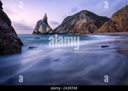 Epische Ursa Strand, Sintra, Portugal. Strand mit Wellen und jugged Rock Peak in Abend weichen Abendlicht. Atlantik Küste Landschaft Stockfoto