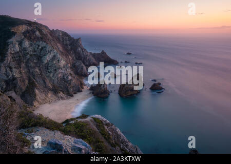 Sonnenuntergang über eine versteckte surreale Praia Da Ursa Strand. Cabo da Roca mit Licht - Haus im Hintergrund. Atlantikküste, Portugal, Europa Stockfoto