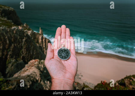 Auf der Suche nach dem Kompass in der Hand palm symbolling Abenteuer - auf der Suche nach Konzept gegen das Meer und die Wellen an die Küste im Hintergrund Stockfoto
