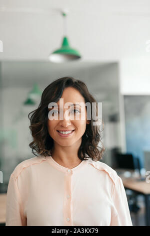 Lächelnden jungen Geschäftsfrau, stehende, sich selbst in einem modernen Büro Stockfoto