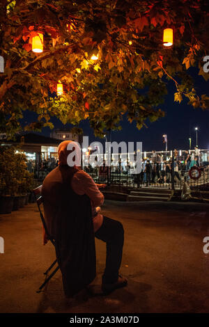 Istanbul: das Nachtleben in der Stadt, eine türkische Frau auf einem Stuhl unter einem Baum mit bunten Laternen dekoriert sitzt und umschließen ein Baby in den Straßen Stockfoto