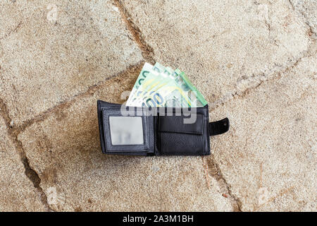 Verloren schwarzes Leder-Etui mit Geld Euro auf die Straße. Ein hundertstel Banknoten innerhalb es Stockfoto