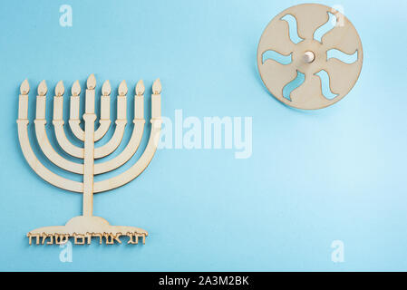 Kinder- Handwerk - Holz menorah Standleuchter und hölzerne dreidels Kreisel Symbole jüdische Feiertag Hanukkah auf blauem Hintergrund. Im Hebräischen happy Hanukah geschrieben, gemütliches Licht. Stockfoto