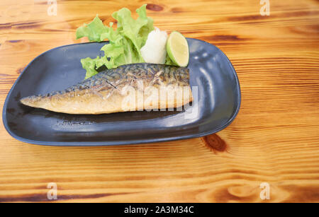 Gegrillte Saba oder Makrele Fisch mit in Scheiben geschnittenen Limetten Obst und geriebenem Meerrettich, Japanisch Meeresfrüchte mit grünem Salat auf einer schwarzen Platte, asiatische Lebensmittel mit braunen nicht Stockfoto