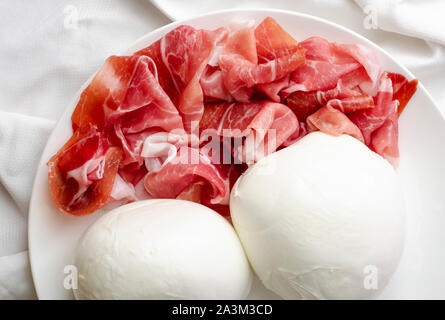 Zwei große Mozzarella Kugeln und Prosciutto Crudo oder jamon auf einem weißen Teller. Nahaufnahme von leckeres italienisches Essen Stockfoto