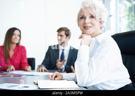 Portrait von lächelnden business Frau sitzt im Büro und suchen an der Kamera. Gerne ältere Frau mit Ihrem Unternehmen zufrieden. Stockfoto