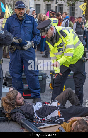 Whitehall, London, UK. 9. Oktober 2019. Große Polizei Präsenz macht Verhaftungen und entfernt vom Aussterben Rebellion Aktivistinnen, die sich an Whitehall geklebt haben. Officer liest einen Abschnitt 14 öffentliche Ordnung handeln, Mitteilung an zwei Demonstranten auf der Straße. Credit: Malcolm Park/Alamy Leben Nachrichten. Stockfoto