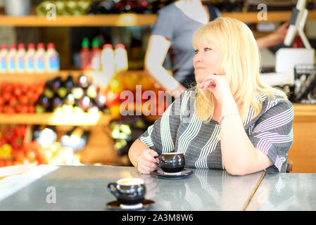 Schöne plus Größe allein Frau trinkt Kaffee an veganen Cafe. Portrait von reife Frau in einer Kantine trinken heißen Cappuccino. Hübsche Frau mittleren Alters mit Tasse Kaffee. Stockfoto