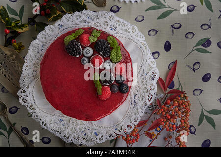 Käsekuchen mit Himbeeren und Brombeeren, Heidelbeeren, Himbeeren und Minze garniert. Auf einem bunten Tischdecke, Blätter und Beeren. Stockfoto