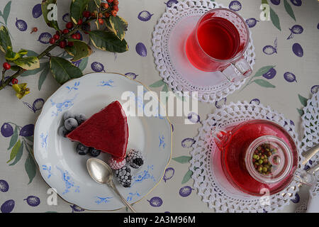 Käsekuchen mit Himbeeren und Brombeeren, Heidelbeeren, Himbeeren und Minze garniert. Auf einem bunten Tischdecke, Blätter und Beeren. Stockfoto