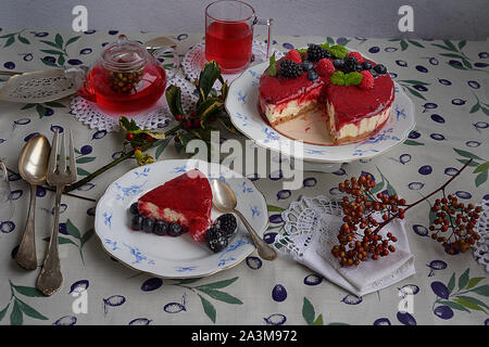 Käsekuchen mit Himbeeren und Brombeeren, Heidelbeeren, Himbeeren und Minze garniert. Auf einem bunten Tischdecke, Blätter und Beeren. Stockfoto