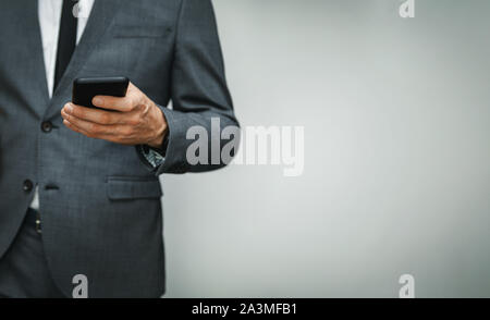Unternehmer tragen mit Phone auf grauem Hintergrund. Kopieren Sie Platz Stockfoto