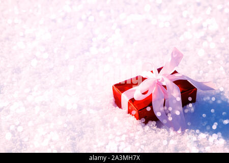 Geschenkverpackung auf rotem Papier und Pink Ribbon mit Lichtern auf Schnee Hintergrund gewickelt. Weihnachten und Neujahr feier Konzept. Stockfoto