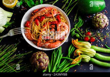 Leckere italienische Pasta mit Tiger Garnelen oder Shrimps und frisches Gemüse auf schwarzem Hintergrund. Gesunde mediterrane Küche Konzept. Stockfoto