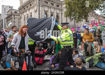 Westminster, London, Großbritannien. Oktober 2019. Aktivisten der Extinction Rebellion nehmen an der Oktoberaufstandsbewegung vor der Methodist Central Hall in London teil. Sie sitzen auf der Straße mit Campingausrüstung und inszenieren einen friedlichen Sitzplatz, während Polizisten ein ausklappbares Zelt demontieren. Die Szene reflektiert Meinungsverschiedenheiten, Umweltaktivismus und polizeiliches Engagement während einer längeren Demonstration im Zentrum Londons. Penelope Barritt/Alamy Live News Stockfoto
