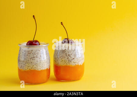 Desserts aus Mango und Chia Milchreis mit Kirschen auf der Oberseite auf gelbem Hintergrund. Kopieren Sie Platz. Gesundes Frühstück Konzept. Stockfoto