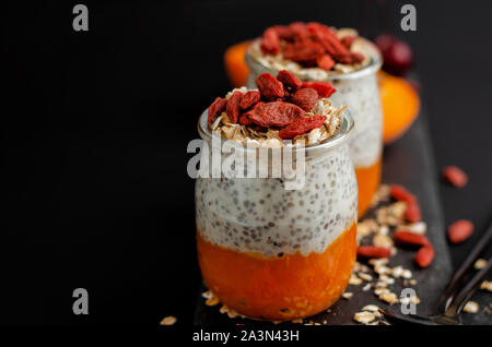 In der Nähe von Chia Samen Pudding mit Goji Beeren, frisch Aprikosen und Hafer essen auf aslate Board auf schwarzen Hintergrund mit kopieren. Gesunden Bala Stockfoto