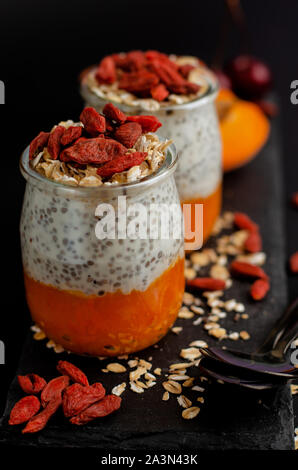 In der Nähe von Chia Samen Pudding mit Goji Beeren, frisch Aprikosen und Hafer essen auf schwarzen Hintergrund mit Kopie Raum, senkrecht. Gesunde, ausgewogene f Stockfoto