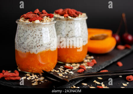 In der Nähe von Chia Samen Pudding mit Goji Beeren, frisch Aprikosen und Hafer essen auf aslate Board auf schwarzen Hintergrund mit kopieren. Gesunden Bala Stockfoto