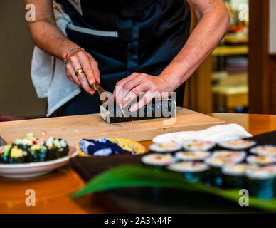 Workshop: Vorbereitung einer Bento-Box in Izunokuni, Japan. Vor dem Hochrollen des Futo Maki Sushi wird die glänzende Seite des Algenblattes nach unten gelegt. Nach jedem Schnitt sollte das Messer mit einem feuchten Tuch gereinigt werden, damit alle Schnitte genau und sauber werden Stockfoto