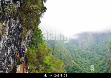 Wanderer Wandern auf einem schmalen Pfad am Rande der Felsen während der levada Caldeirao Verde Trail. Misty Green Mountains im Hintergrund. Gefährliche wandern. Portugiesische touristische Attraktion. Nebel, Nebel. Stockfoto