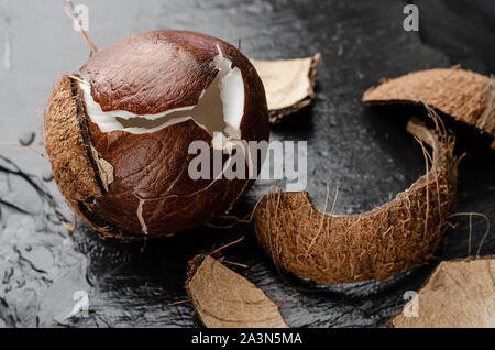 Gebrochene reife Kokosnuss auf schwarzem Schiefer Hintergrund. Gesunde Ernährung Konzept. Stockfoto