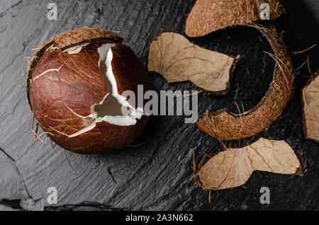 Gebrochene raw Coconut auf schwarzem Schiefer Hintergrund. Diät und vegetarische Kost. Stockfoto