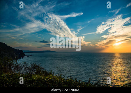 Der Berg Fuji verschwindet unter treibenden Wolkenschleiern am Horizont über Yaizu, die bewaldeten Klippen öffnen sich zum Meer im Vordergrund. Präfektur Shizuoka, Japan. Stockfoto