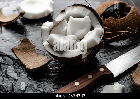 Organische Kokosnuss hlf mit Stücken auf schwarzem Schiefer Hintergrund. Gesunde fettreiche Nahrungsmittel Konzept. Stockfoto