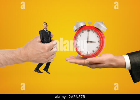 Große männliche Hand vorbei an winzigen Geschäftsmann auf der anderen Seite mit Wecker auf gelbem Hintergrund Stockfoto
