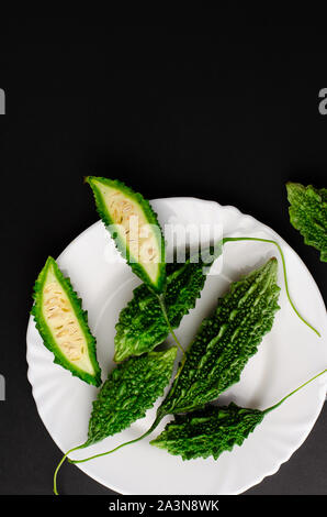 Momordica charanita oder bitter Gurke auf weiße Platte auf schwarzem Hintergrund. Platz kopieren, flach. Stockfoto